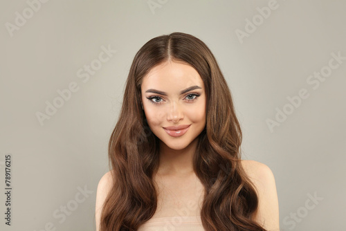 Gorgeous young female model with healthy hair, makeup and shiny clear skin posing against gray studio wall background. Facial treatment, cosmetology, hair care and beauty woman concept