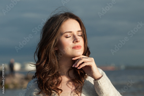 Carefree young lady brunette model on sea beach. Beauty woman with makeup and long dark wavy hairstyle outdoors. Tranquility emotion mood, travel, season and holiday concept