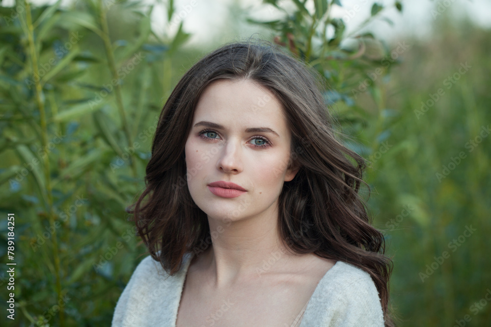 Naklejka premium Close-up portrait of healthy young brunette woman with fresh clear skin and long dark brown hair outdoors on green grass background, air portrait