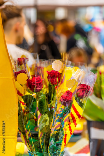 Detail of a bouquet of roses, decorated with ears of wheat and the flag of Catalonia, in a flower and book stall at a traditional festival market with people walking on Sant Jordi's Day.