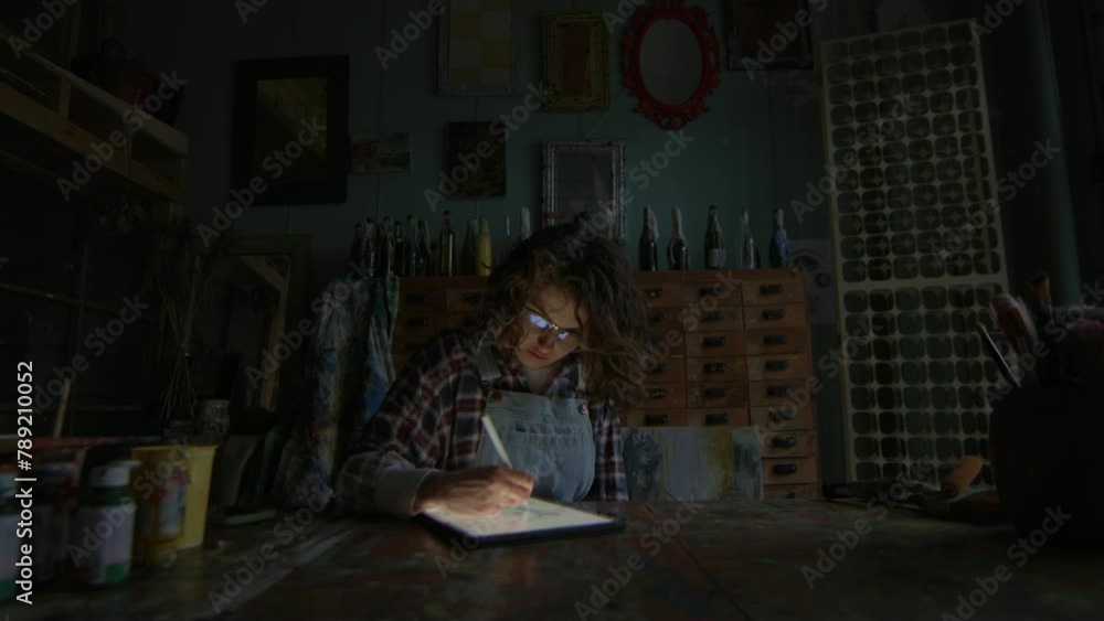 Artist sketching on tablet computer in a dimly lit studio surrounded by art supplies Artist sketching on tablet computer in a dimly lit studio surrounded by art supplies