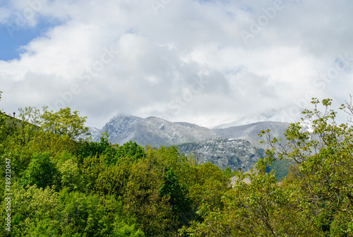 Outdoors, snow-capped mountains in April with green trees