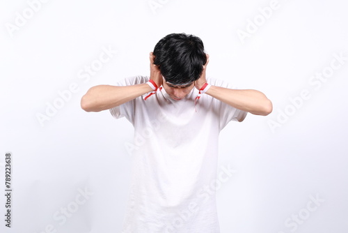 Frustrated asian young boy with red white ribbon for celebrating Indonesia independence day standing while holding head and covering ears