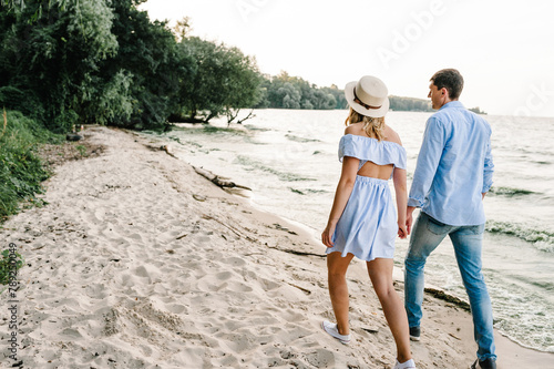 Female and male walk on beach ocean and enjoy sunny summer day on vacation. Man and woman walking on sand sea. Happy couple in love holding hands go on seashore. Spending time together. Back view.