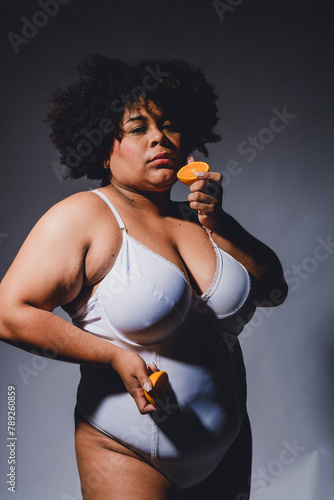 waist up portrait of young afrolatina woman posing in lingerie holding an orange fruit in hands