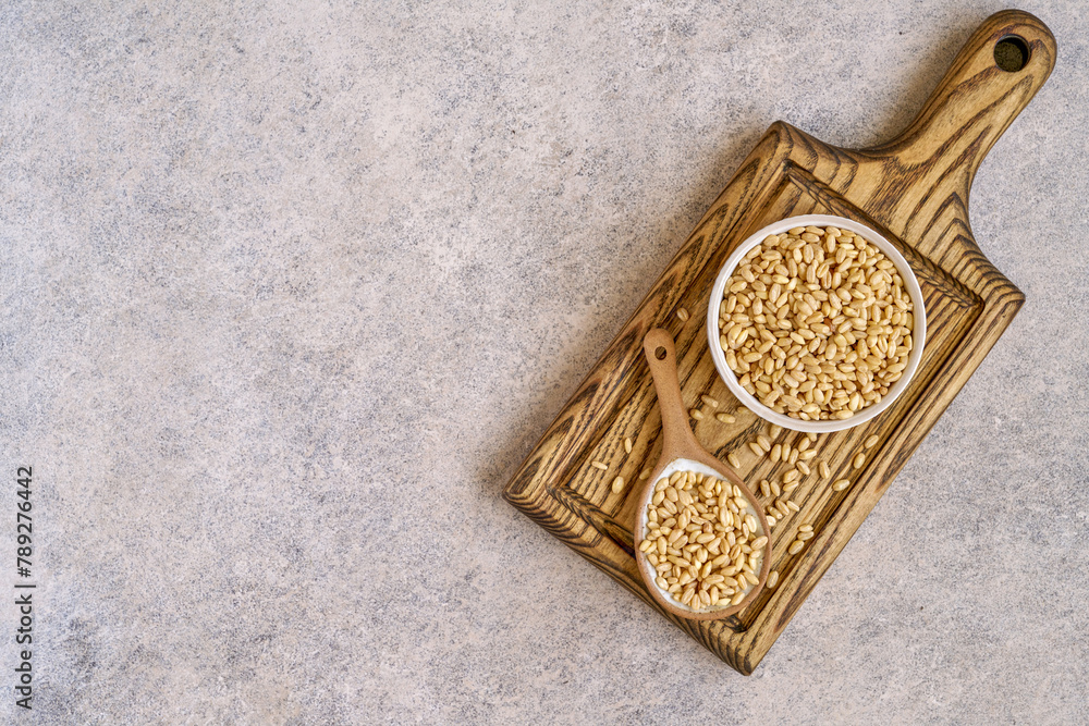 Wheat grains in ceramic bowl and spoon on wooden board. Top view Wheat grains in ceramic bowl and spoon on wooden board. Top view