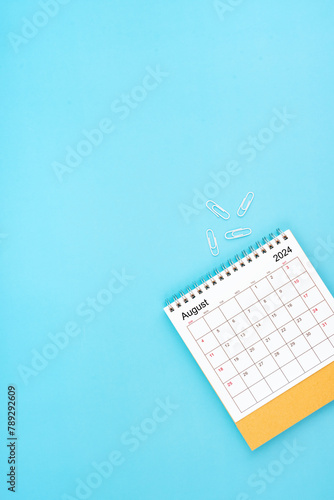Desk calendar for August 2024 and white paper clip on a light blue.