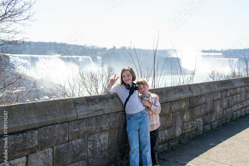 Tourists, them back to the camera, looking into the tower view at the Niagara Falls from the Canadian side, city visible in background; slightly cloudy sky. High quality photo