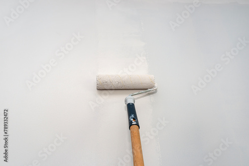 Painter paints a room in beige color using a paint roller on an extended stick at home.