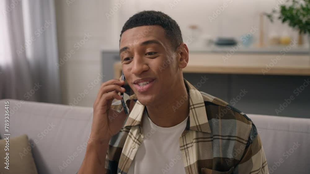 Smiling African American ethnic man carefree guy smile male talking call smartphone talk speaking mobile phone speak communicate laughing conversation gadget at home couch sofa chatting glad happy Smiling African American ethnic man carefree guy smile male talking call smartphone talk speaking mobile phone speak communicate laughing conversation gadget at home couch sofa chatting glad happy