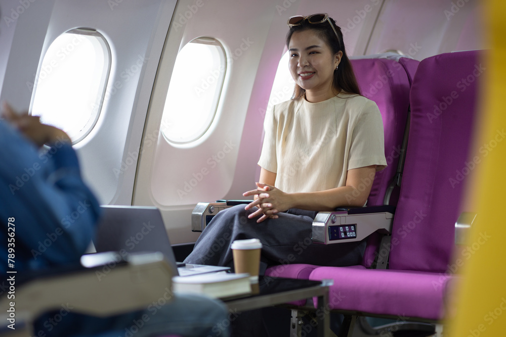 Young Asian woman and friends sitting talking and taking travel photos while in flight. Young female tourists and friends enjoying an amazing trip in Asia use their mobile phone to take a photo.