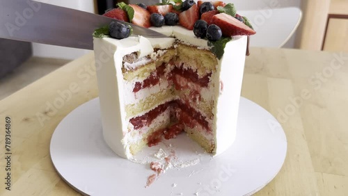 White cut cake with strawberry filling and decorate by strawberry and blueberry close up. Big beautiful cake for  birthday. Care cut and it is seen all teasty layers of cream, biscuit and jem photo