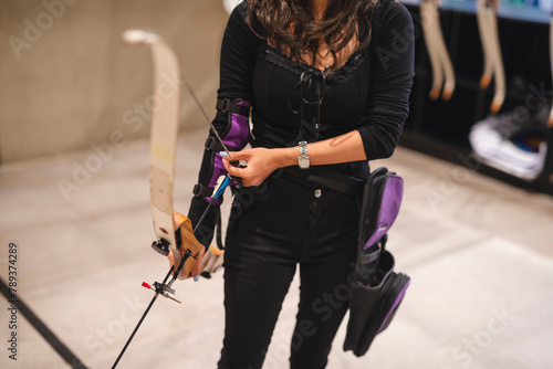 Fotografie Anonymous shot of a beginner Asian woman practices archery at an indoor range, exploring a new hobby