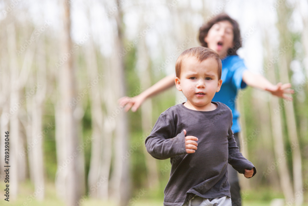 Toddler running towards the camera with an older child running behind him. Toddler running towards the camera with an older child running behind him.