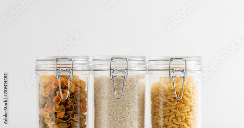 food storage, eating and cooking concept - close up of jars with rice and pasta on white background