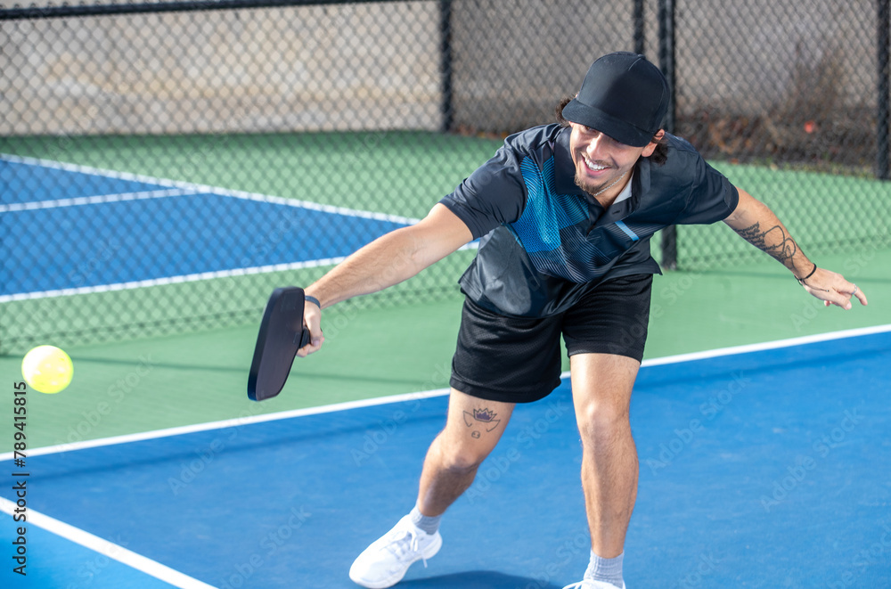 Man playing pickleball hits the ball with his paddle while in a game on an outdoor court. Man playing pickleball hits the ball with his paddle while in a game on an outdoor court.