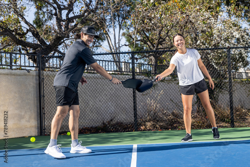 Co-Ed pickleball team playing a game together outside. The man and woman are athletic and working well as a team in the popular sport. They are tapping paddles like a high five.  photo