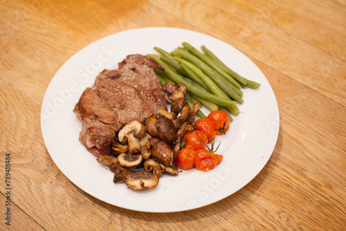 A rib eye steak served with mushrooms, tomatoes and green beans