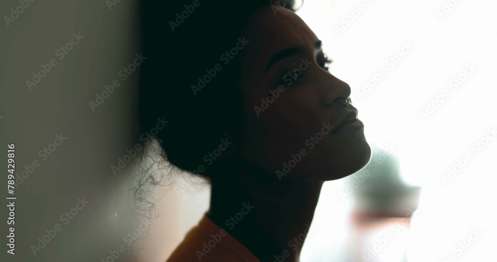 One depressed young black latina woman leaning on wall with melancolic expression gazing at distance feeling lost in thought, profile close-up face in silhouette One depressed young black latina woman leaning on wall with melancolic expression gazing at distance feeling lost in thought, profile close-up face in silhouette