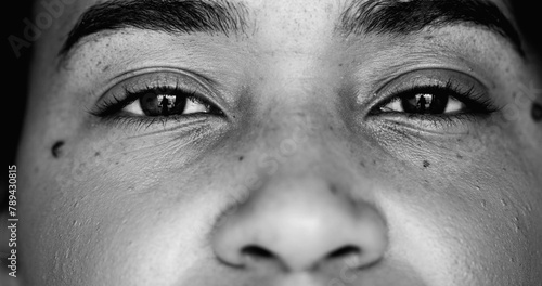Intense macro close-up face of one young black woman facial eyesight features in monochrome, black and white gaze at camera photo
