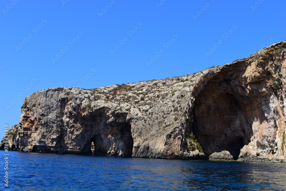 ZURRIEQ, MALTA - Augusts 06, 2021: The Blue Grotto - A famous sea cave surrounded by the deep blue sea at southern Malta. On a traditional boat surrounded by more brightly coloured boats. 