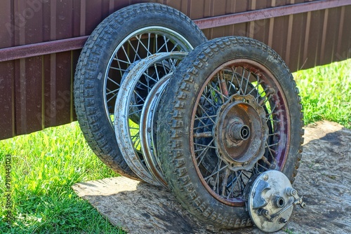 four rusty iron wheels with spokes and black rubber tires, discarded wheels from a retro motorcycle stand on the ground near an iron brown fence on the street during the day photo