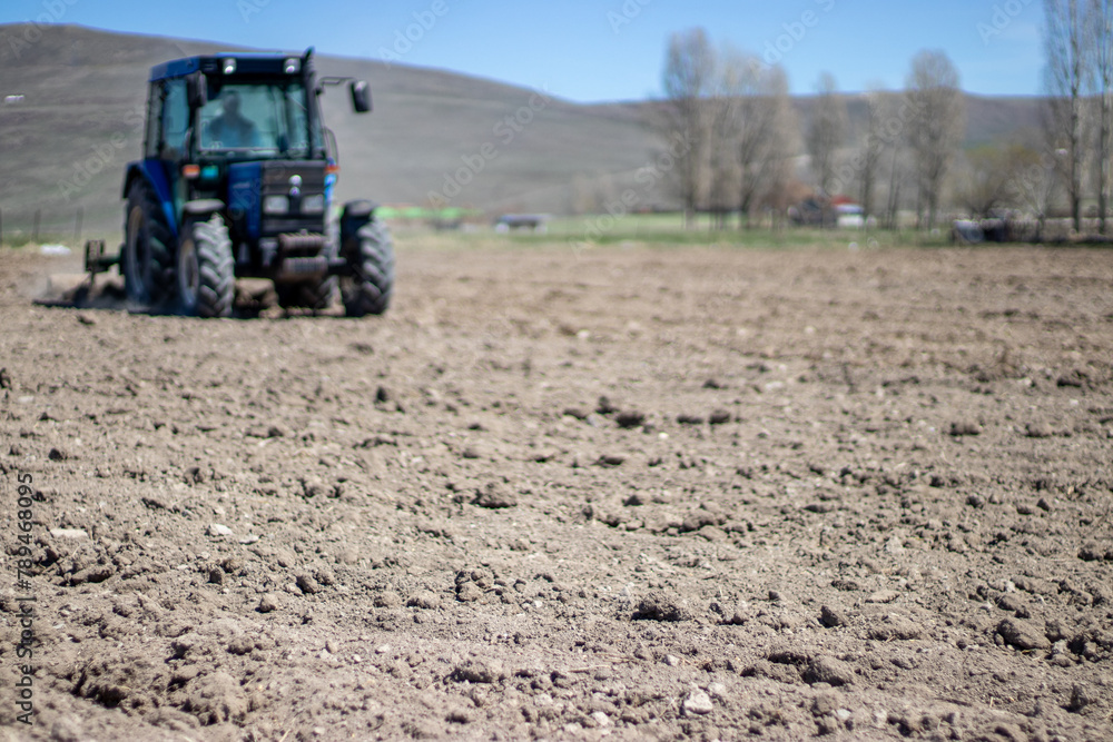 Focused on cultivating the land, this image captures a tractor plowing a field, readying the soil for spring planting against a pastoral backdrop Focused on cultivating the land, this image captures a tractor plowing a field, readying the soil for spring planting against a pastoral backdrop
