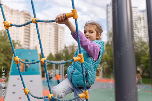 Cheerful girl 6 years old climbing the rope ladder, children's sport at playground