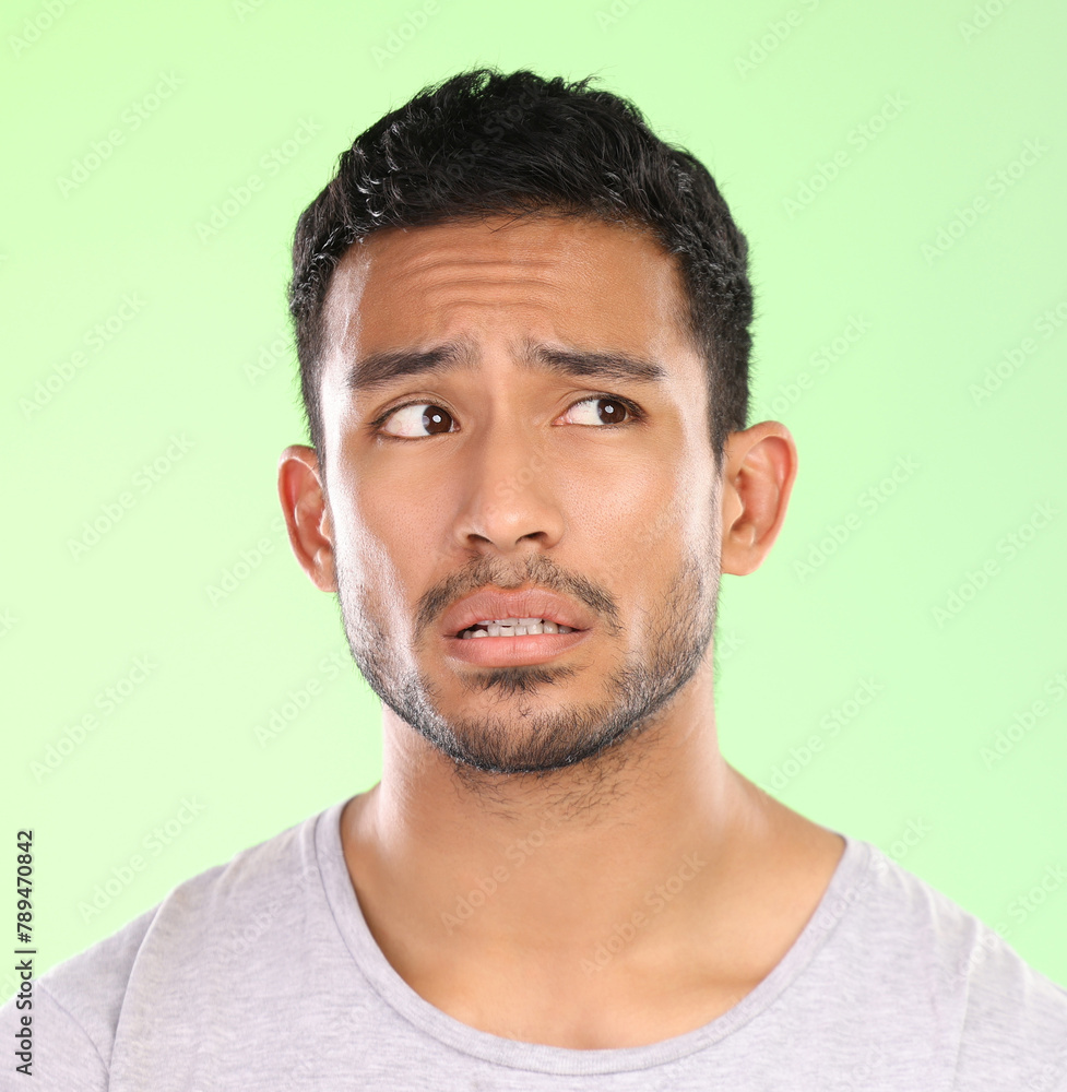 Obraz premium Confused man, thinking and unsure with wonder in doubt, question or uncertainty on a green studio background. Face of male person or worried model in thought, ponder or curious for idea or decision