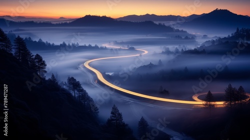 Long exposure captures the serpentine flow of headlights winding through a foggy pine valley at sunset, a mystic scene