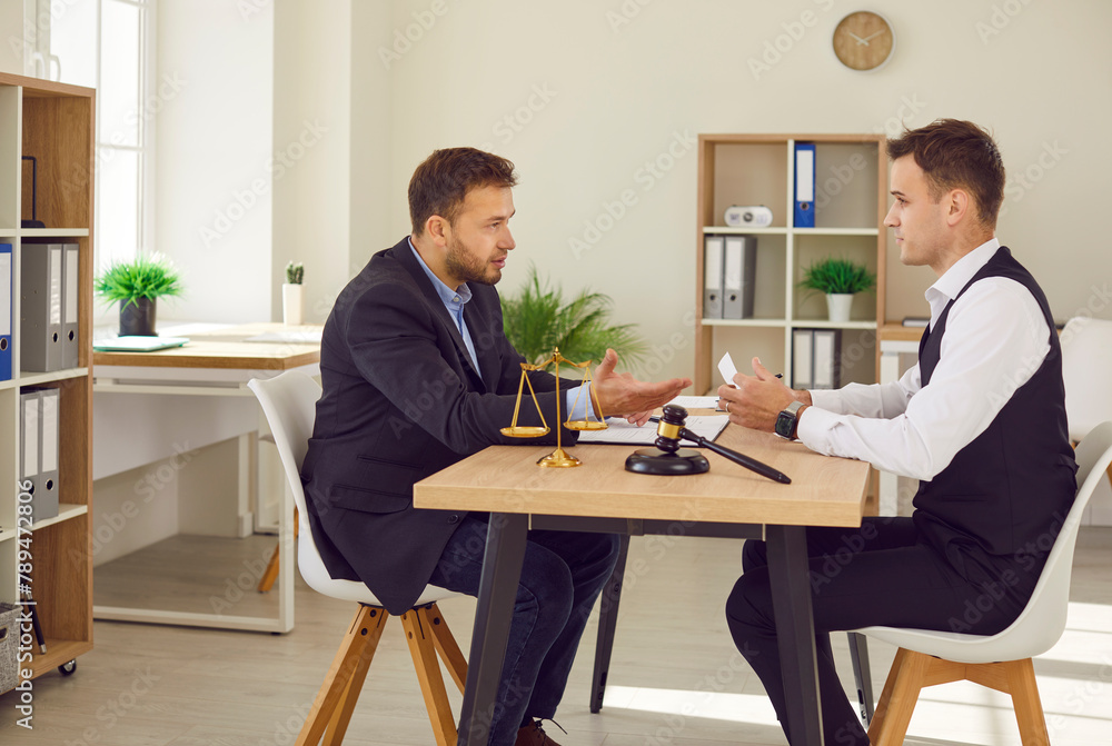 Male lawyer working on his workplace in office having discussion during consultation with man client sitting at the desk with judge's gavel and scales on table. Legal law and advice concept.