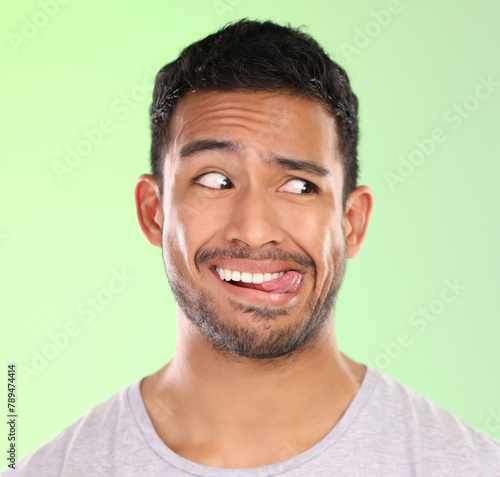 Man, play and silly in studio, tongue and goofy comic or funny face on green background. Male person, mockup space and awkward for joke or comedy, student and humor for crazy character and quirky