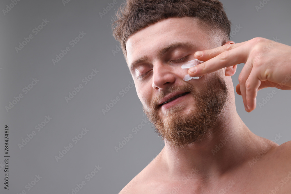 Obraz premium Handsome man applying moisturizing cream onto his face on grey background, space for text