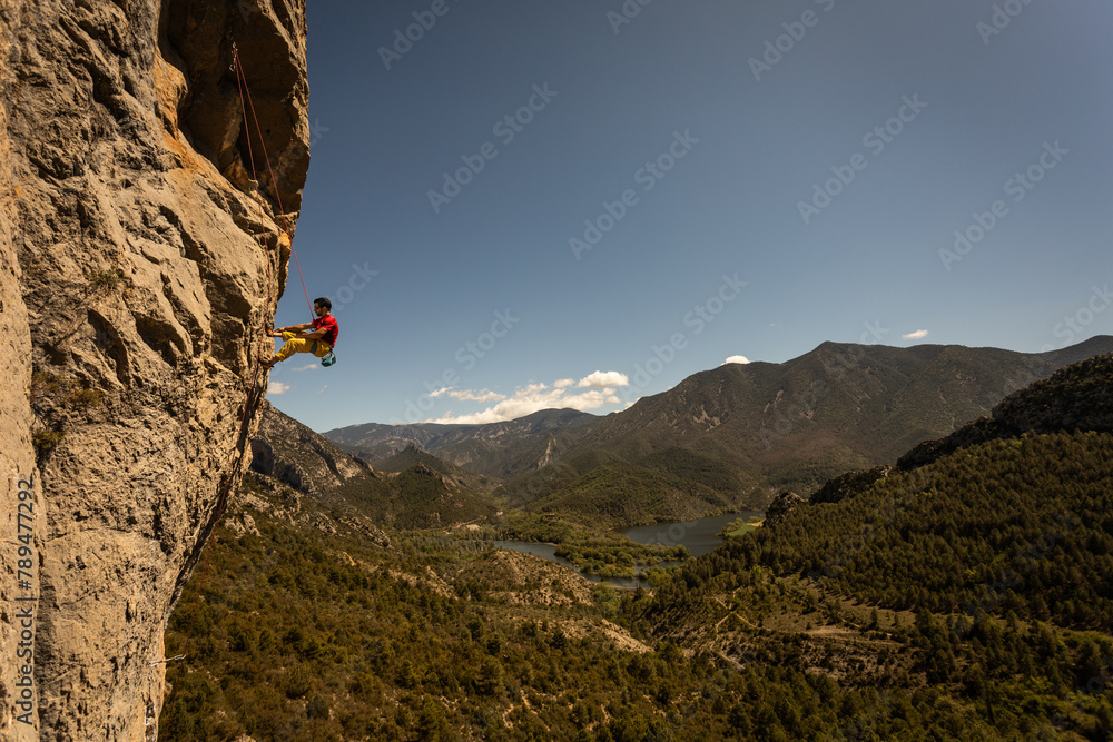 A man is climbing a rock face with a view of mountains in the background. The scene is serene and peaceful, with the man's focus on the climb and the beauty of the surrounding landscape