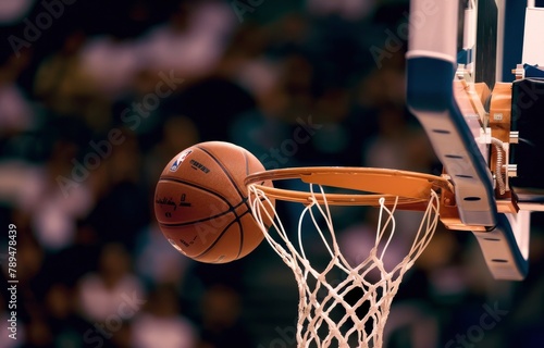 A closeup of a basketball passing through the net with the background of the audience fuzzily visible.