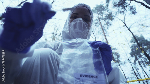 Woman forensic expert works at a crime scene, collecting evidence in a plastic bag, focusing on the investigation  photo