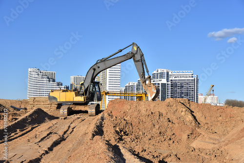 Construction site. Excavator on groundwork. Backhoe dig foundation for house construction. Building construction, renovation. Excavator on earthworks for road construction. Tower crane in build.