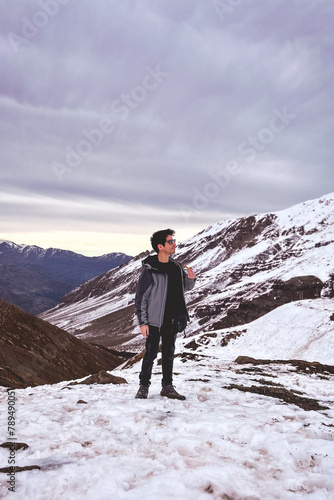 High altitude chill: young man enjoys a serene cannabis smoke from a pipe on a snowy mountain peak with panoramic views