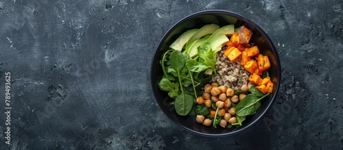Top-down view of a black bowl containing a salad made with avocado, quinoa, sweet potato, spinach, and chickpeas, with empty space for text.