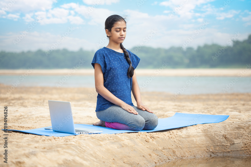 young fitness women doing vajrasana yoga in the tranquility beach using laptop