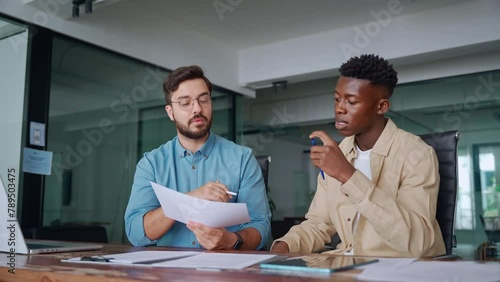 Professional young business man manager financial advisor consulting client having conversation sitting at work meeting. Two busy diverse male employees checking documents talking in office.