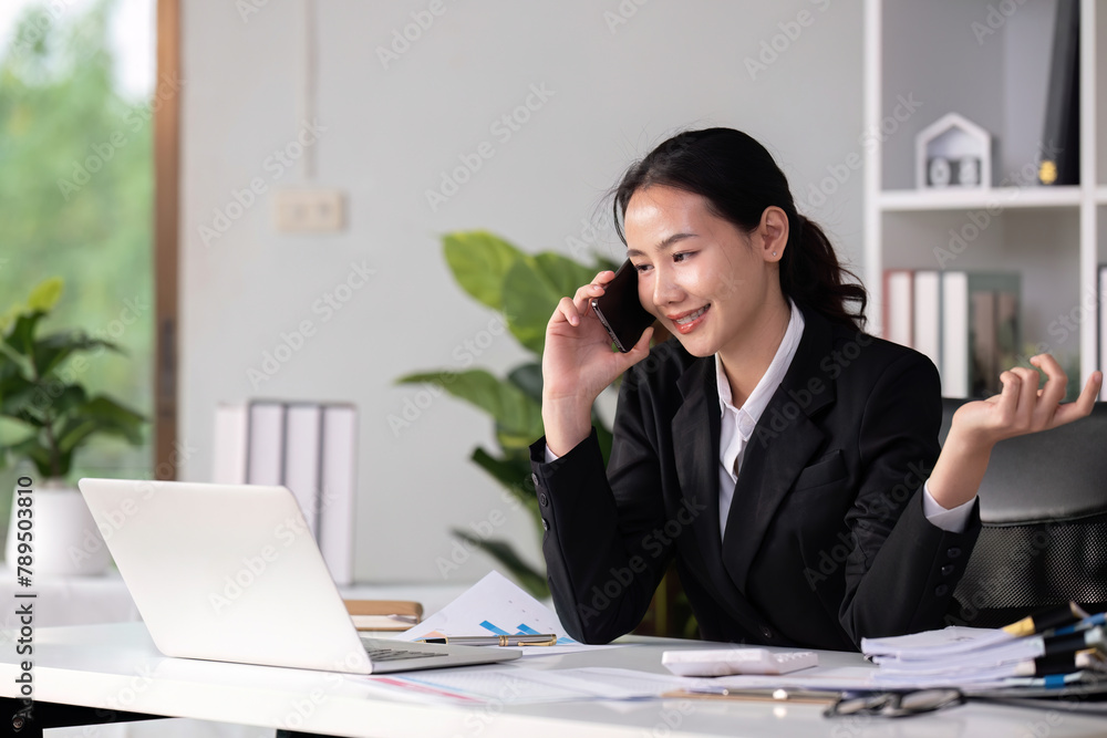 Asian female accountant Discussing business over the phone in an office with work plan documents on the table Asian female accountant Discussing business over the phone in an office with work plan documents on the table