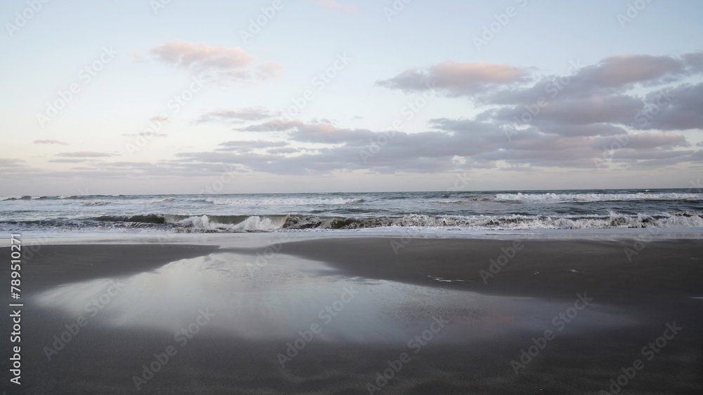 Panorama view of the ocean waves and beach under a sunset sky. The landscape reflection in the water. 