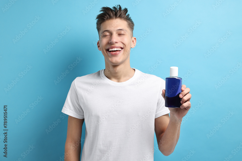 Young man with mouthwash on light blue background Young man with mouthwash on light blue background