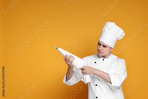 Portrait of confectioner in uniform holding piping bag on orange background, space for text photo