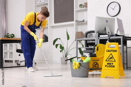 Cleaning service worker washing floor with mop. Bucket with supplies and wet floor sign in office photo