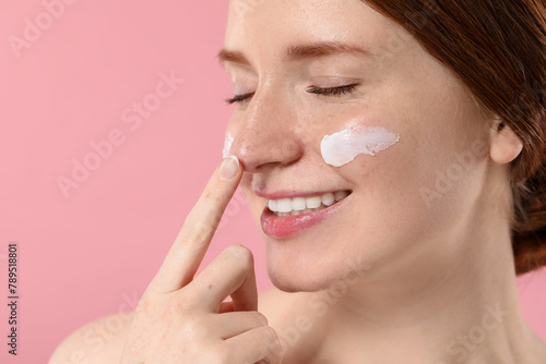 Smiling woman with freckles and cream on her face against pink background, closeup. Space for text