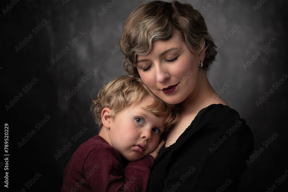 Young mother holding and hugging her little boy who is a toddler child with curly blond hair and blue eyes