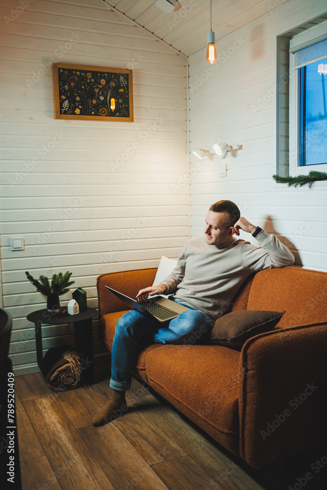 A handsome man in home clothes sits on a sofa and works on a laptop. Remote freelance work. A handsome man in home clothes sits on a sofa and works on a laptop. Remote freelance work.