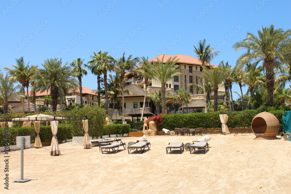 A sandy beach with palm trees and a building with blue sky